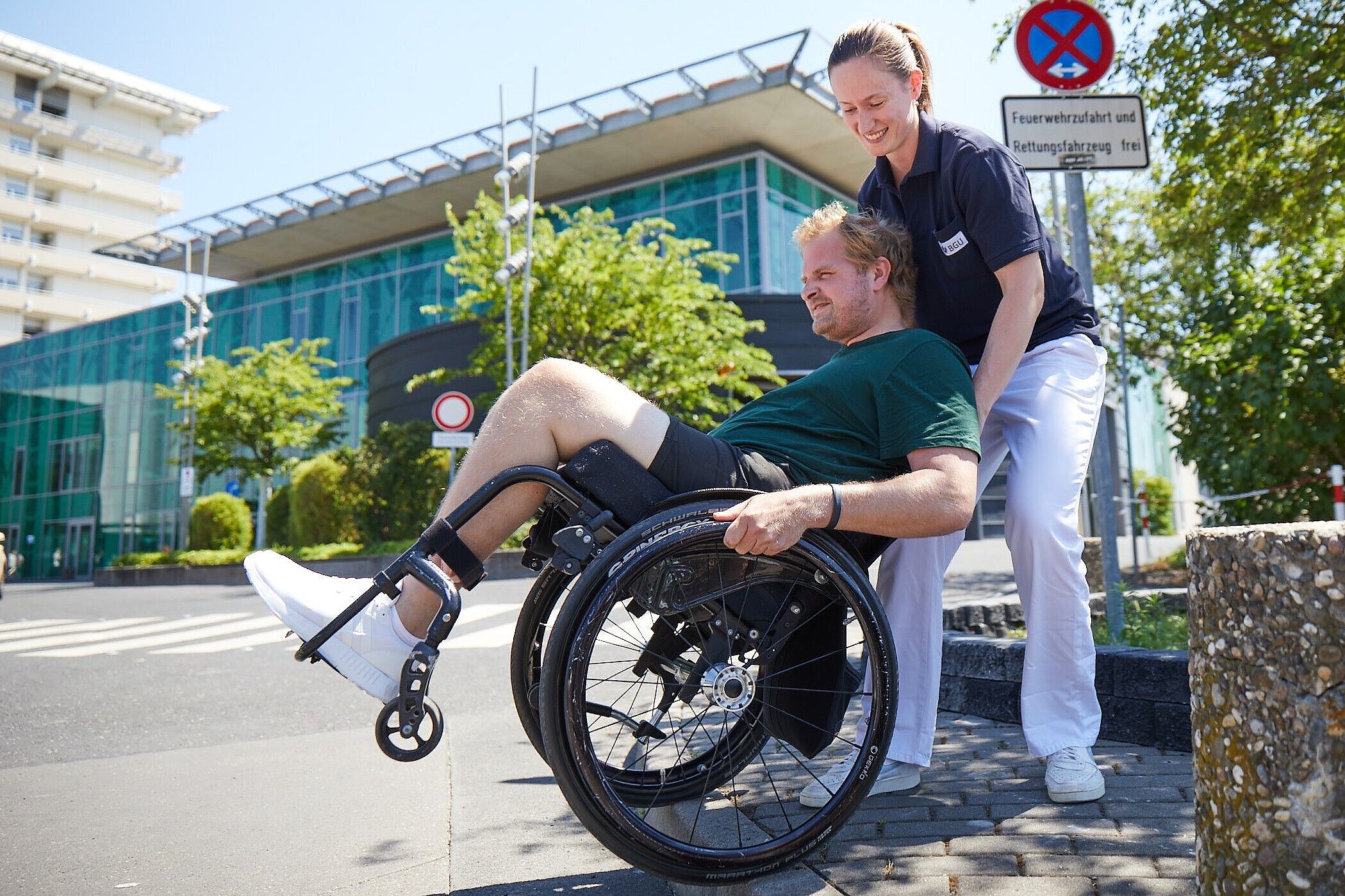 Tag der Therapie Therapeutin mit einem Patienten im Rollstuhl vor Klinikgebäude